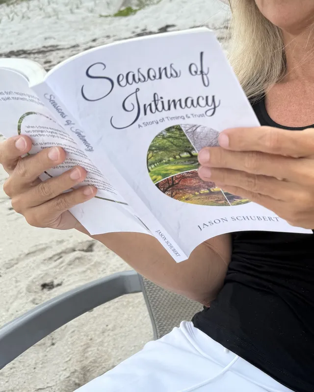 A reader holding Seasons of Intimacy open on the beach