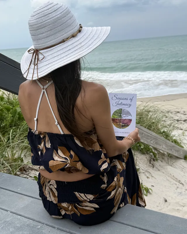 A reader in a sun hat with Seasons of Intimacy, looking out over the dunes